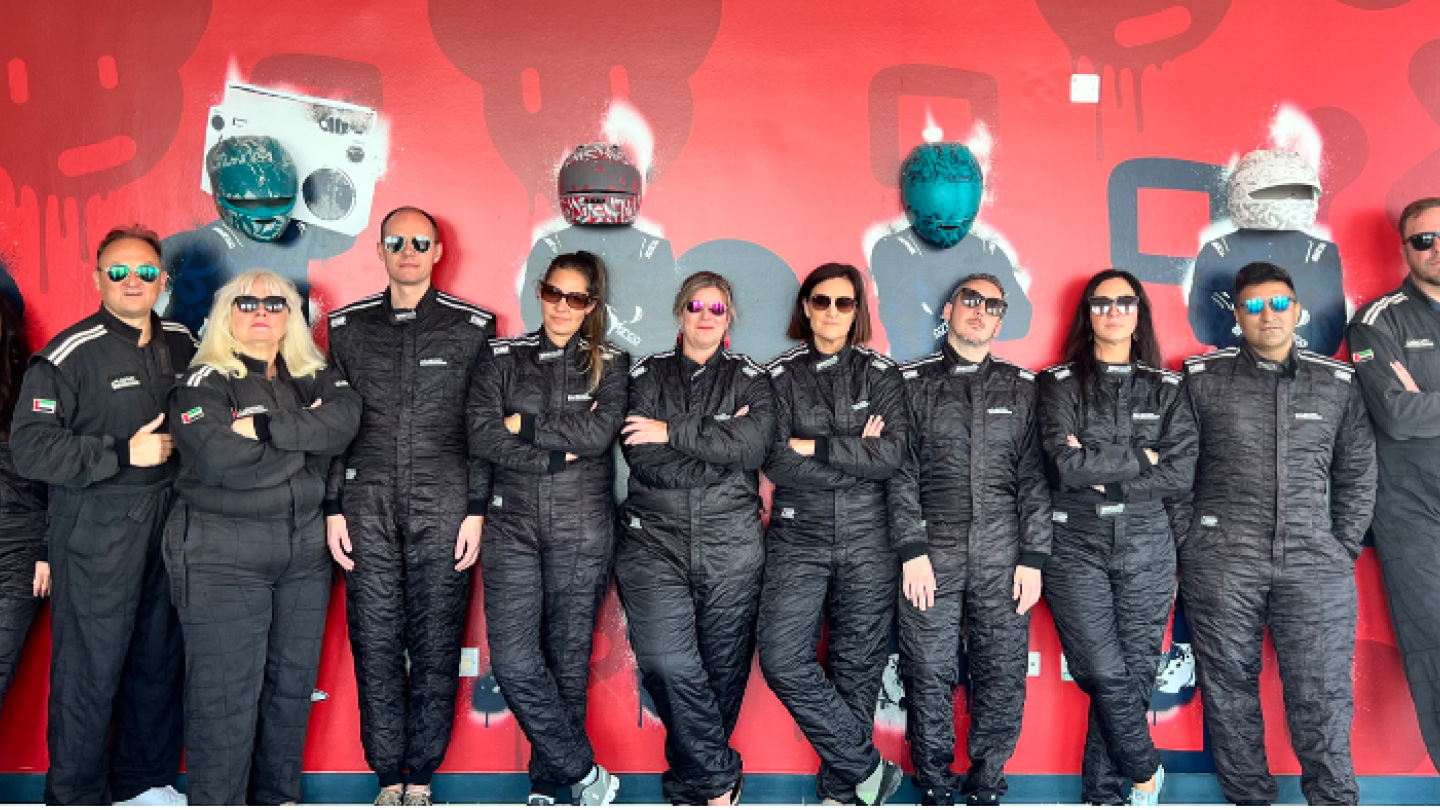 The SITE board of directors is lined up in black tracksuits against a red background, onsite at the go-kart track